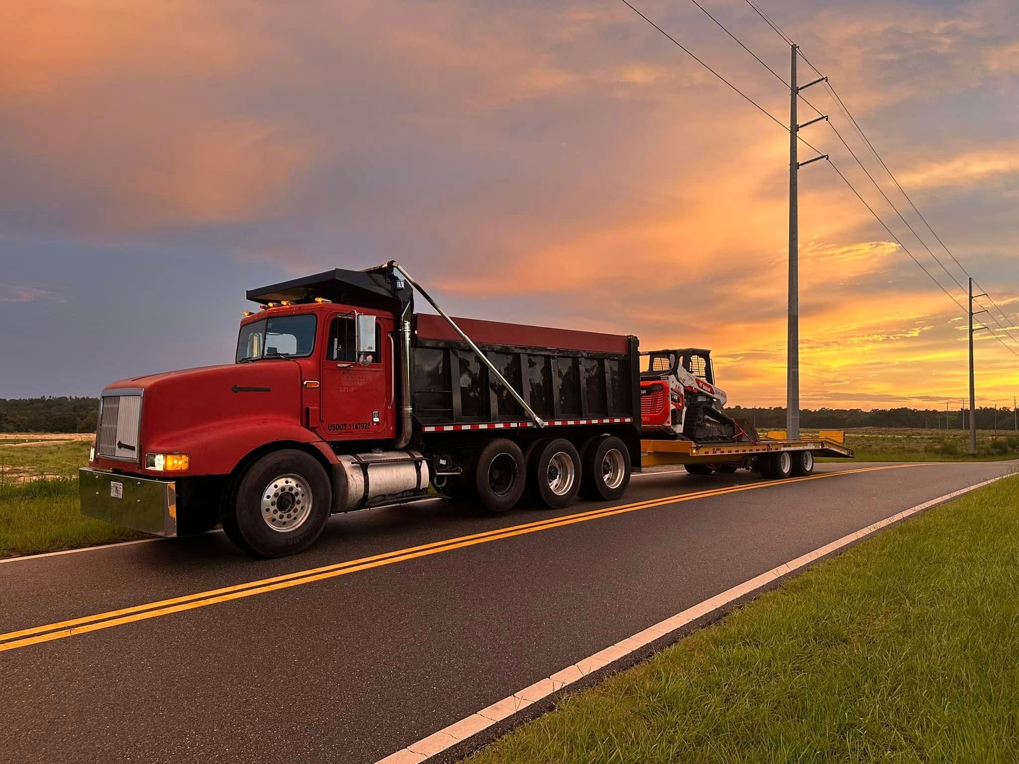 Mintel Land Management fleet heading out at sunset, red dump truck, lowboy trailer, and skid steer on a Central Florida highway